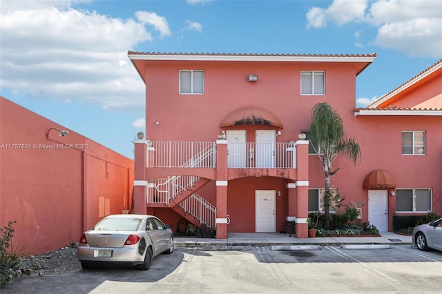 view of front of home featuring stairs, uncovered parking, a tiled roof, and stucco siding