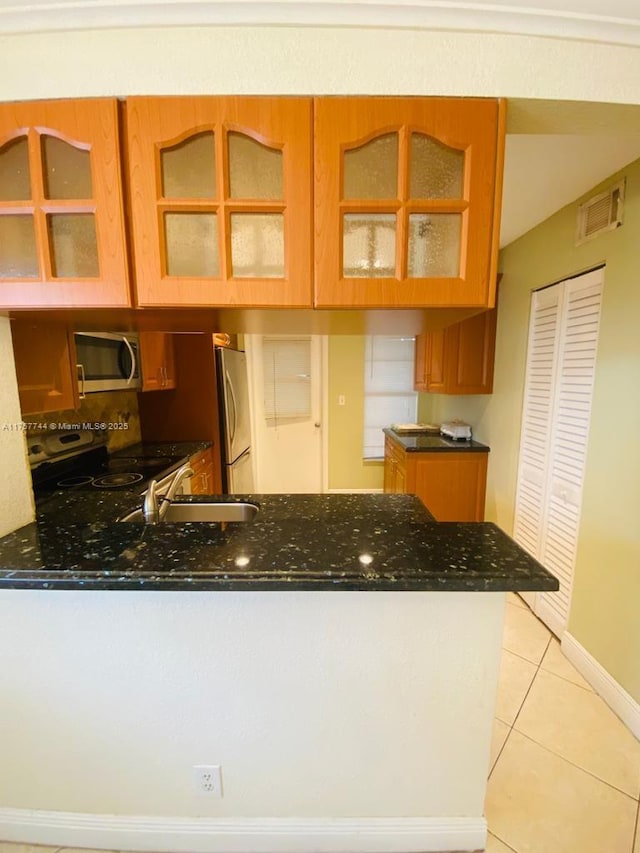 kitchen with light tile patterned floors, visible vents, appliances with stainless steel finishes, glass insert cabinets, and a peninsula