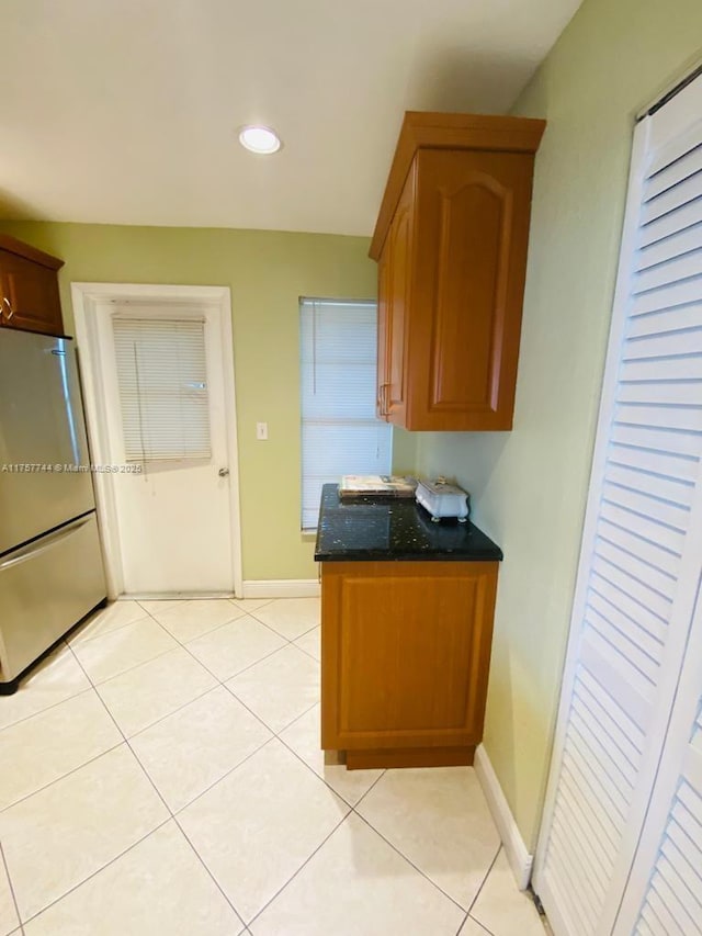 kitchen featuring light tile patterned floors, dark stone counters, stainless steel fridge, and baseboards