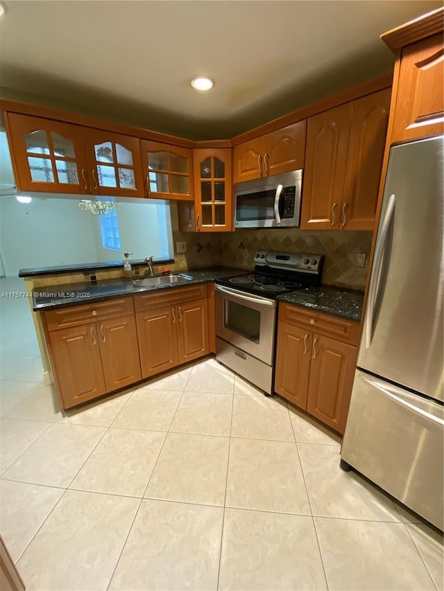 kitchen featuring light tile patterned floors, tasteful backsplash, glass insert cabinets, appliances with stainless steel finishes, and a sink