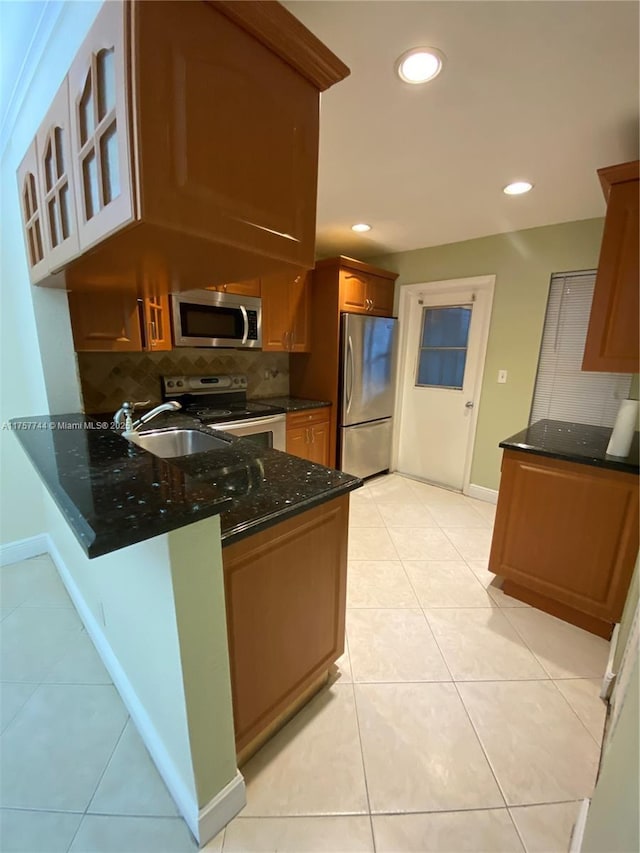 kitchen featuring light tile patterned flooring, stainless steel appliances, a peninsula, decorative backsplash, and dark stone countertops