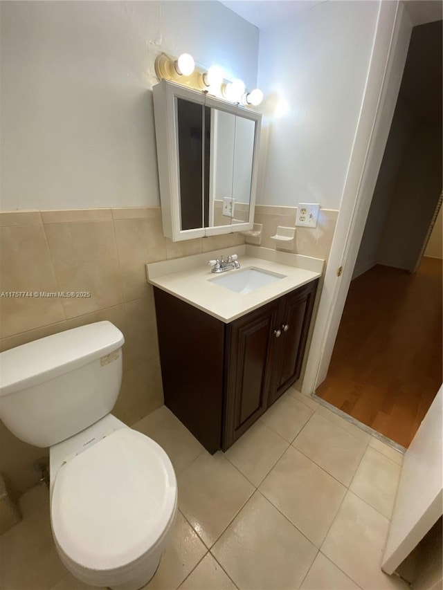 bathroom with toilet, vanity, tile patterned flooring, and tile walls