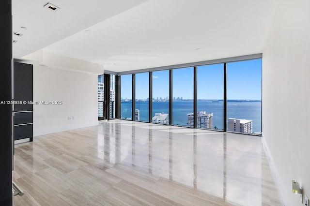 empty room with a water view, expansive windows, and baseboards