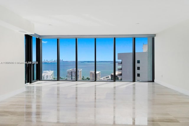 unfurnished room featuring a water view, baseboards, and a wall of windows