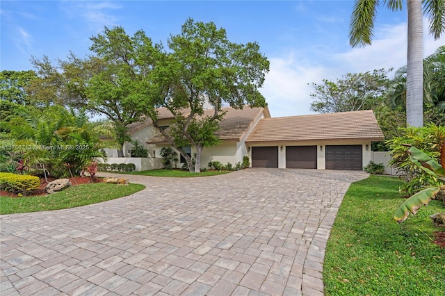 view of front of home with a tiled roof, an attached garage, fence, decorative driveway, and stucco siding