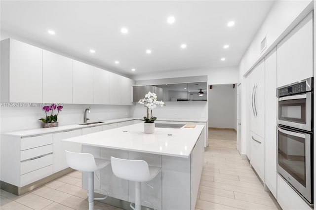 kitchen with light countertops, stainless steel double oven, a kitchen island, a sink, and modern cabinets