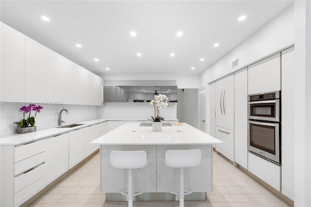 kitchen with visible vents, modern cabinets, a center island, double oven, and a sink