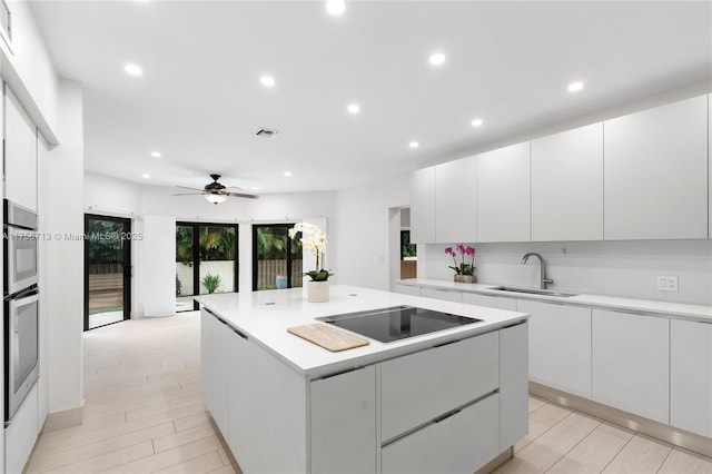 kitchen featuring visible vents, a kitchen island, black electric stovetop, light countertops, and a sink