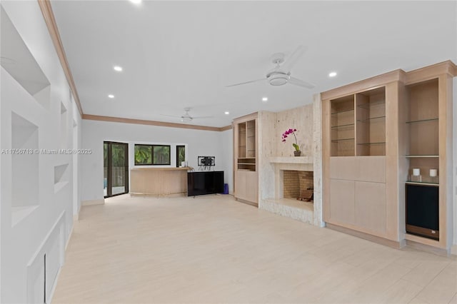 unfurnished living room with a large fireplace, ceiling fan, built in shelves, and ornamental molding