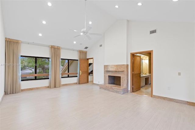 unfurnished living room with high vaulted ceiling, a premium fireplace, light wood-type flooring, and visible vents