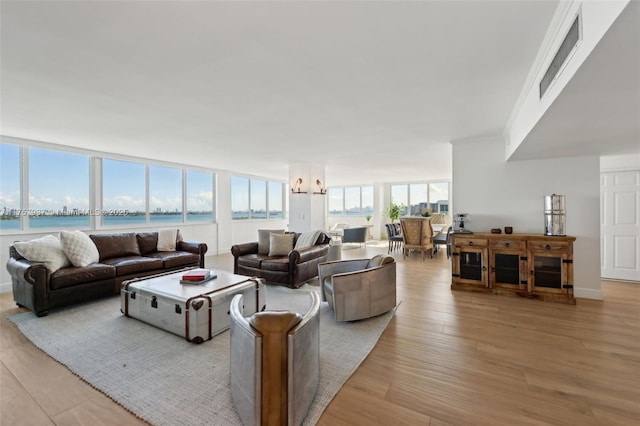 living room with a water view, visible vents, baseboards, light wood-type flooring, and crown molding