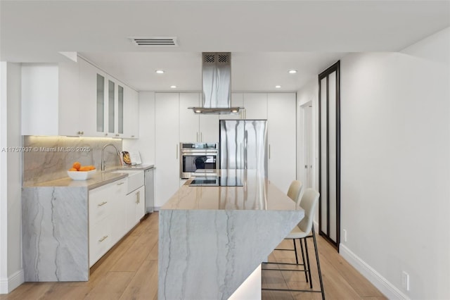 kitchen with island range hood, a kitchen island, modern cabinets, stainless steel appliances, and a sink