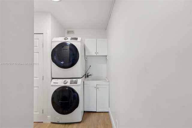 clothes washing area featuring a sink, stacked washer and dryer, light wood-type flooring, and cabinet space