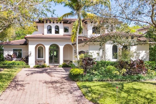 mediterranean / spanish house featuring a tiled roof, decorative driveway, french doors, a front lawn, and stucco siding