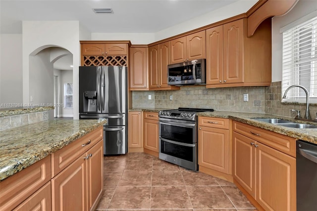 kitchen featuring visible vents, light stone counters, appliances with stainless steel finishes, a sink, and backsplash