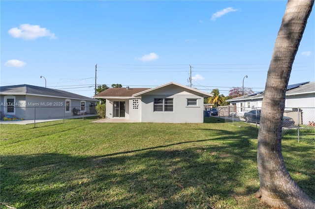 rear view of property with a lawn, fence, and stucco siding