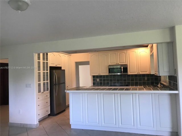 kitchen with tile counters, decorative backsplash, appliances with stainless steel finishes, light tile patterned flooring, and a peninsula