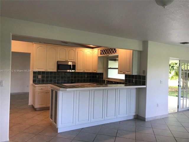 kitchen featuring visible vents, decorative backsplash, tile counters, stainless steel microwave, and a peninsula