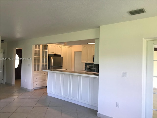 kitchen featuring visible vents, decorative backsplash, freestanding refrigerator, a peninsula, and light tile patterned flooring