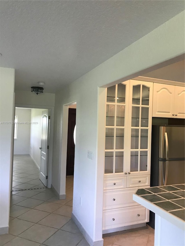 kitchen with glass insert cabinets, freestanding refrigerator, white cabinets, and a textured ceiling