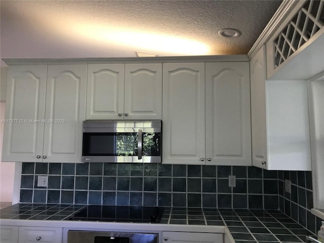 kitchen with stainless steel microwave, white cabinets, and tile counters