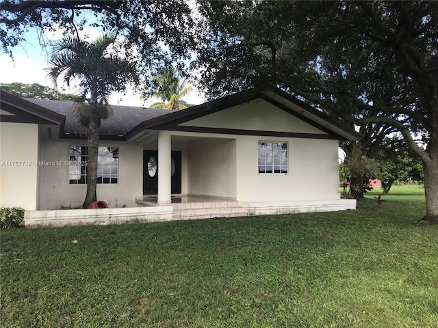 rear view of property with a shingled roof, a lawn, and stucco siding