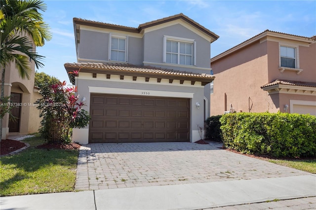 mediterranean / spanish home featuring decorative driveway, a tiled roof, an attached garage, and stucco siding