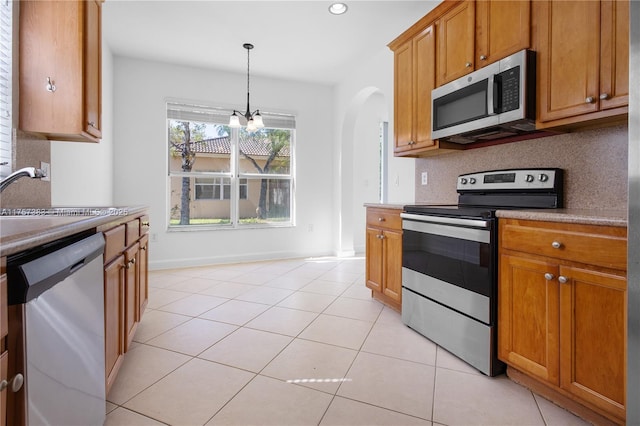 kitchen featuring tasteful backsplash, brown cabinetry, stainless steel appliances, a sink, and light tile patterned flooring