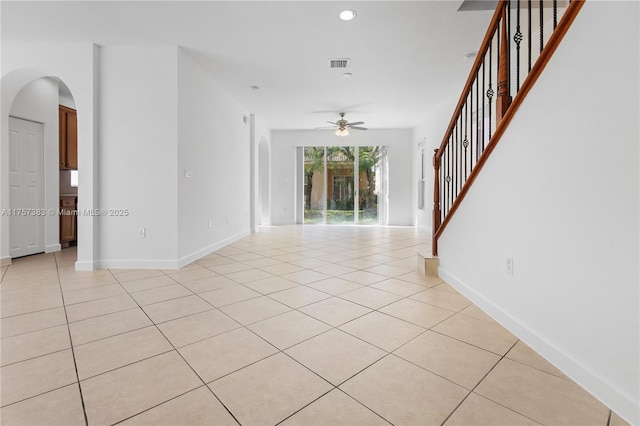 spare room featuring light tile patterned floors, baseboards, visible vents, arched walkways, and stairway