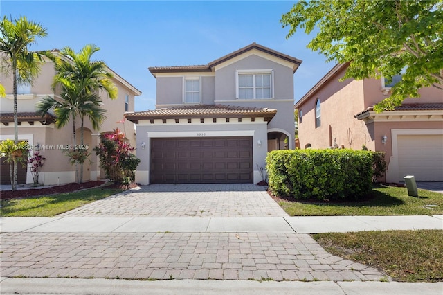 mediterranean / spanish home featuring a garage, a tiled roof, decorative driveway, and stucco siding