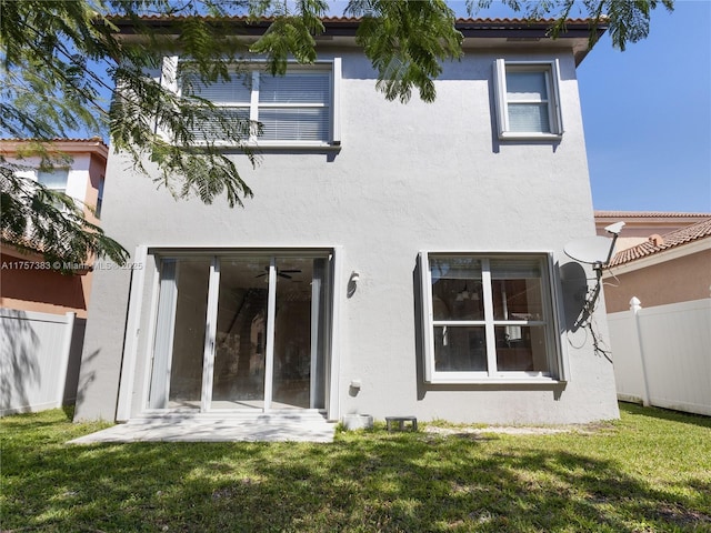 back of house featuring fence, a lawn, and stucco siding