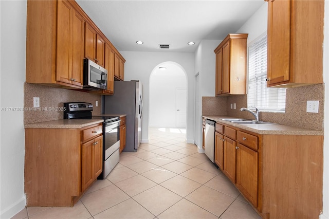 kitchen with arched walkways, light tile patterned floors, stainless steel appliances, a sink, and light countertops