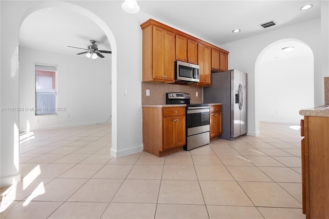 kitchen featuring stainless steel appliances, brown cabinetry, light tile patterned flooring, and tasteful backsplash