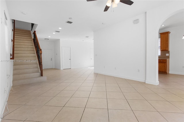 unfurnished living room featuring arched walkways, recessed lighting, light tile patterned flooring, ceiling fan, and stairs