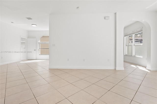 spare room featuring light tile patterned floors, baseboards, visible vents, and arched walkways