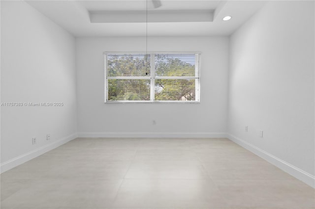 empty room featuring recessed lighting, a raised ceiling, and baseboards