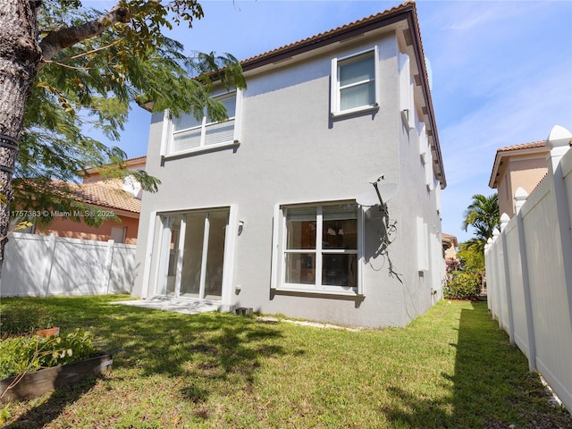 rear view of property featuring fence private yard, a tiled roof, a lawn, and stucco siding