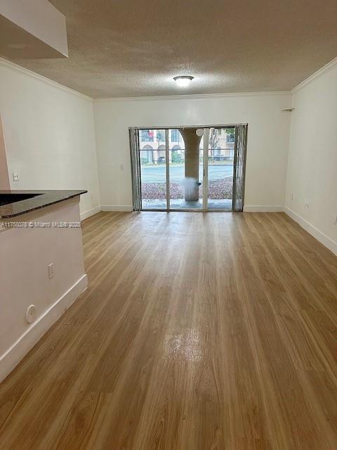 unfurnished living room featuring baseboards, a textured ceiling, ornamental molding, and wood finished floors