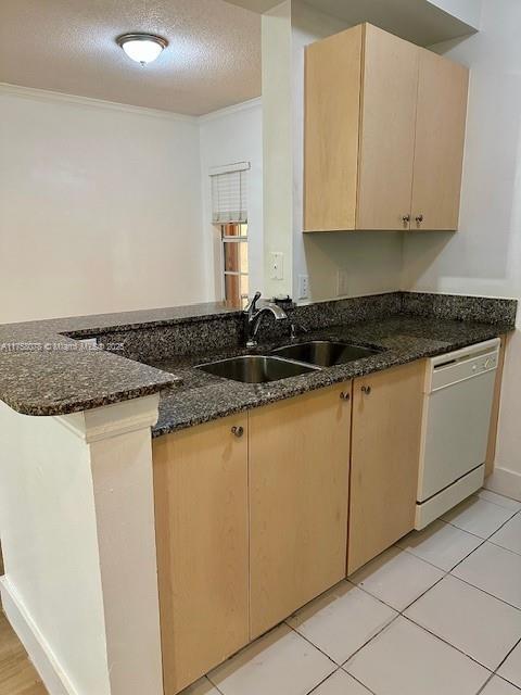 kitchen featuring white dishwasher, a sink, a textured ceiling, dark stone counters, and a peninsula