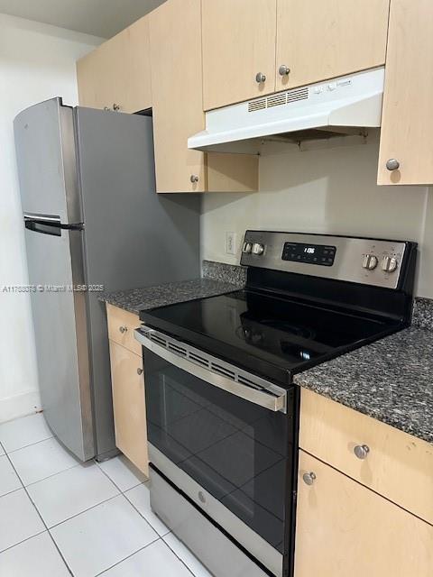 kitchen with appliances with stainless steel finishes, dark stone counters, under cabinet range hood, and light tile patterned floors