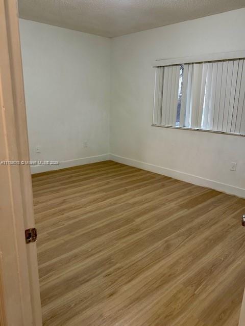 empty room featuring baseboards, a textured ceiling, and light wood-style floors