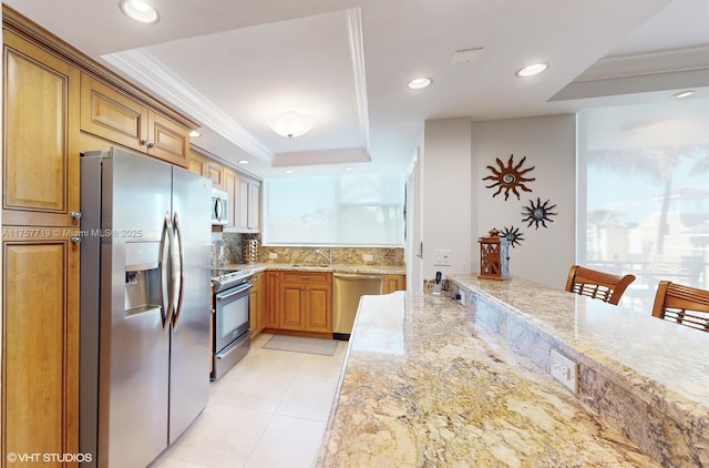 kitchen featuring light tile patterned floors, appliances with stainless steel finishes, light stone counters, a tray ceiling, and crown molding