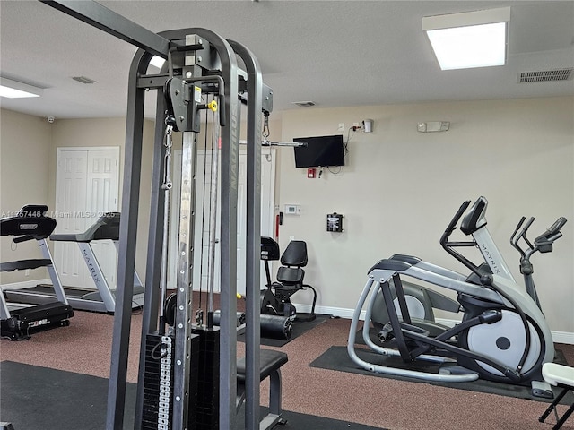 exercise room with visible vents, a textured ceiling, and baseboards