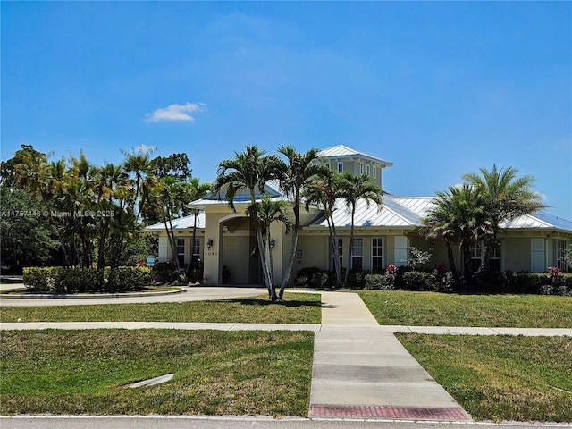 view of front facade featuring a standing seam roof, metal roof, a front lawn, and stucco siding