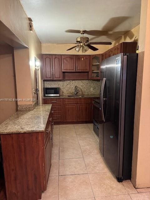 kitchen featuring light tile patterned flooring, a sink, freestanding refrigerator, decorative backsplash, and stainless steel microwave