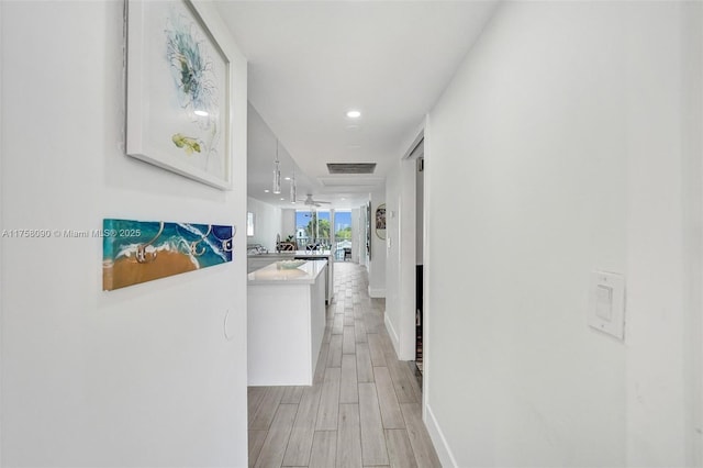 corridor featuring wood tiled floor, visible vents, and baseboards