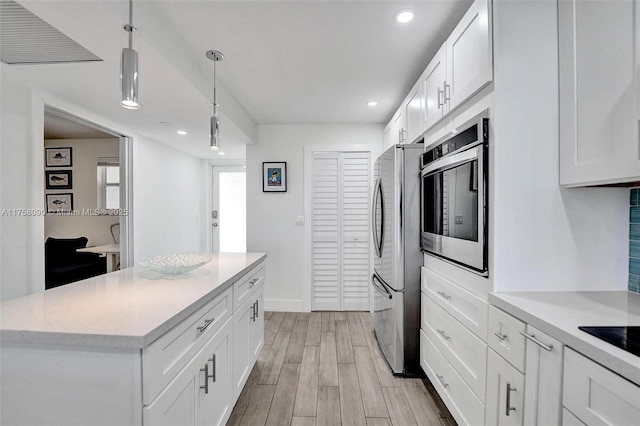 kitchen with white cabinets, appliances with stainless steel finishes, hanging light fixtures, light countertops, and light wood-style floors