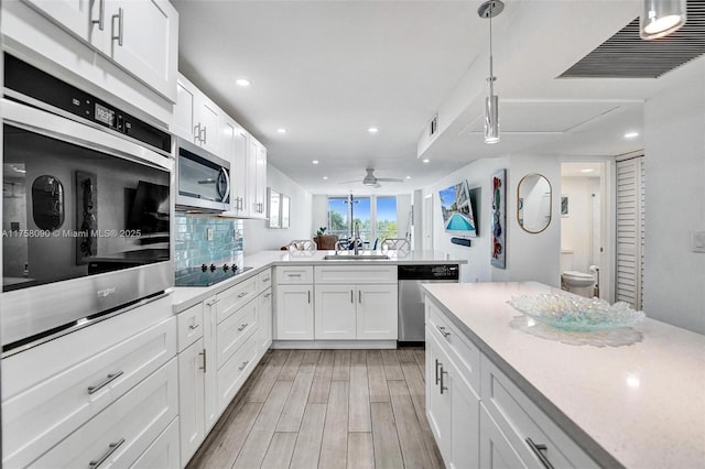 kitchen with light wood finished floors, visible vents, a peninsula, stainless steel appliances, and a sink