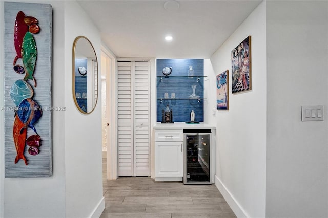 bar with recessed lighting, beverage cooler, baseboards, light wood finished floors, and a bar