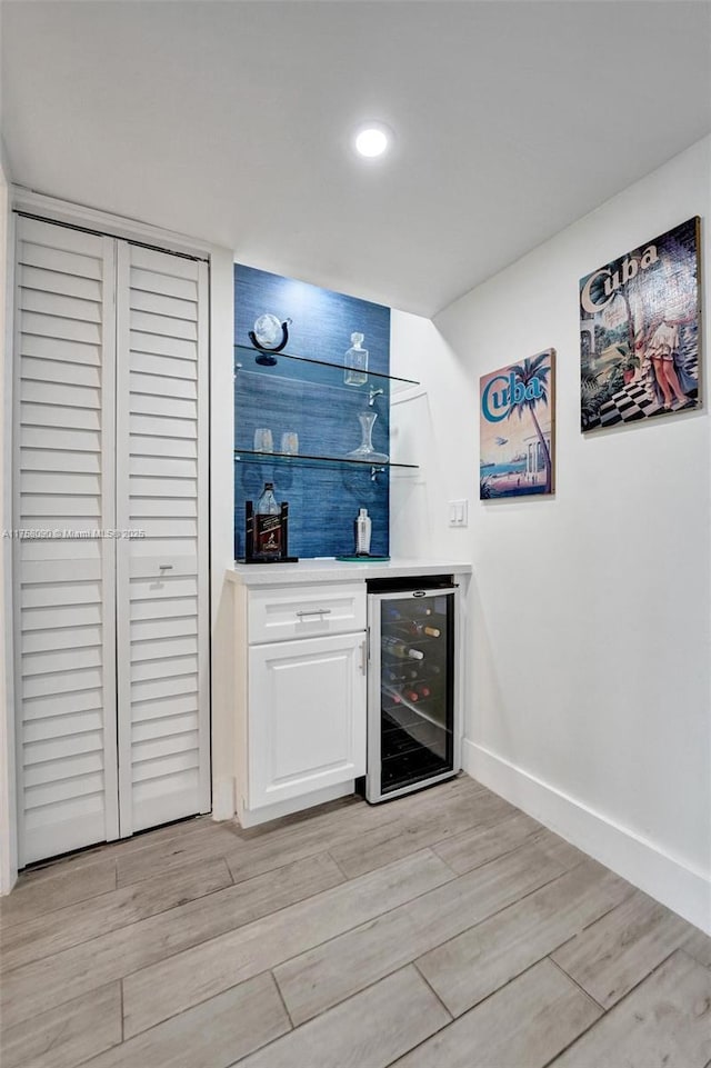 bar featuring a dry bar, light wood-style flooring, wine cooler, and baseboards